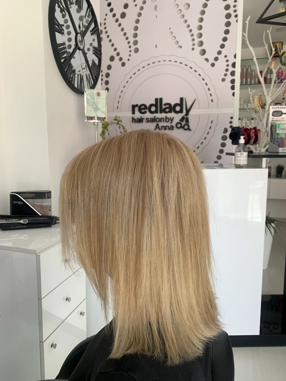 Inside the RedLady salon with the logo wall behind a fresh blonde cut